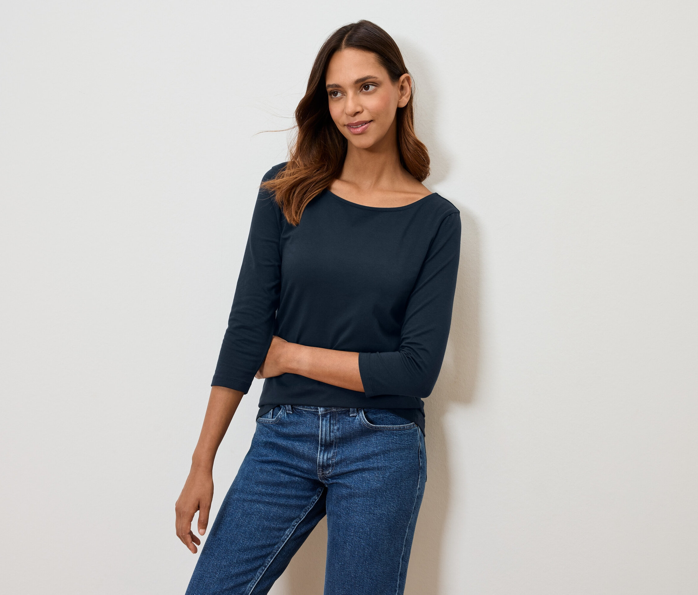 Frau posiert in marineblauem Dreiviertelarm-Shirt und blauen Jeans.