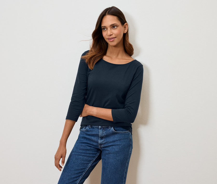 Frau posiert in marineblauem Dreiviertelarm-Shirt und blauen Jeans.