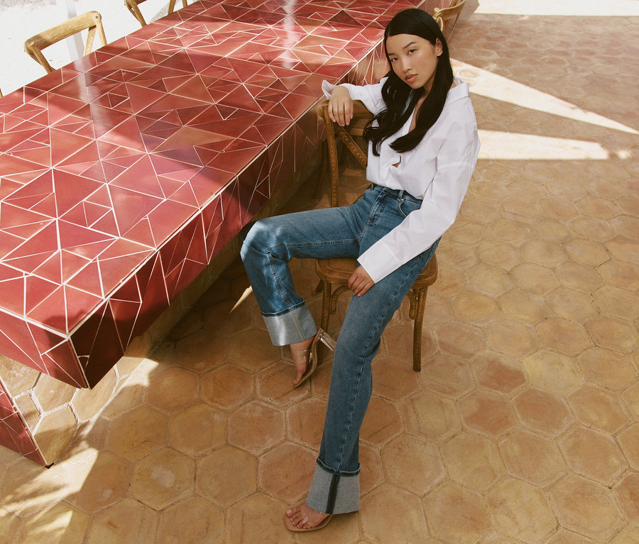 Eine Frau sitzt auf einem Stuhl an einem Tisch und trägt hellblaue Angels Jeans »Lara« Straight Fit Turn Up.