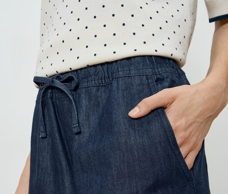 Frau mit Hand in der Tasche eines Jeansrocks mit Kordelzug.