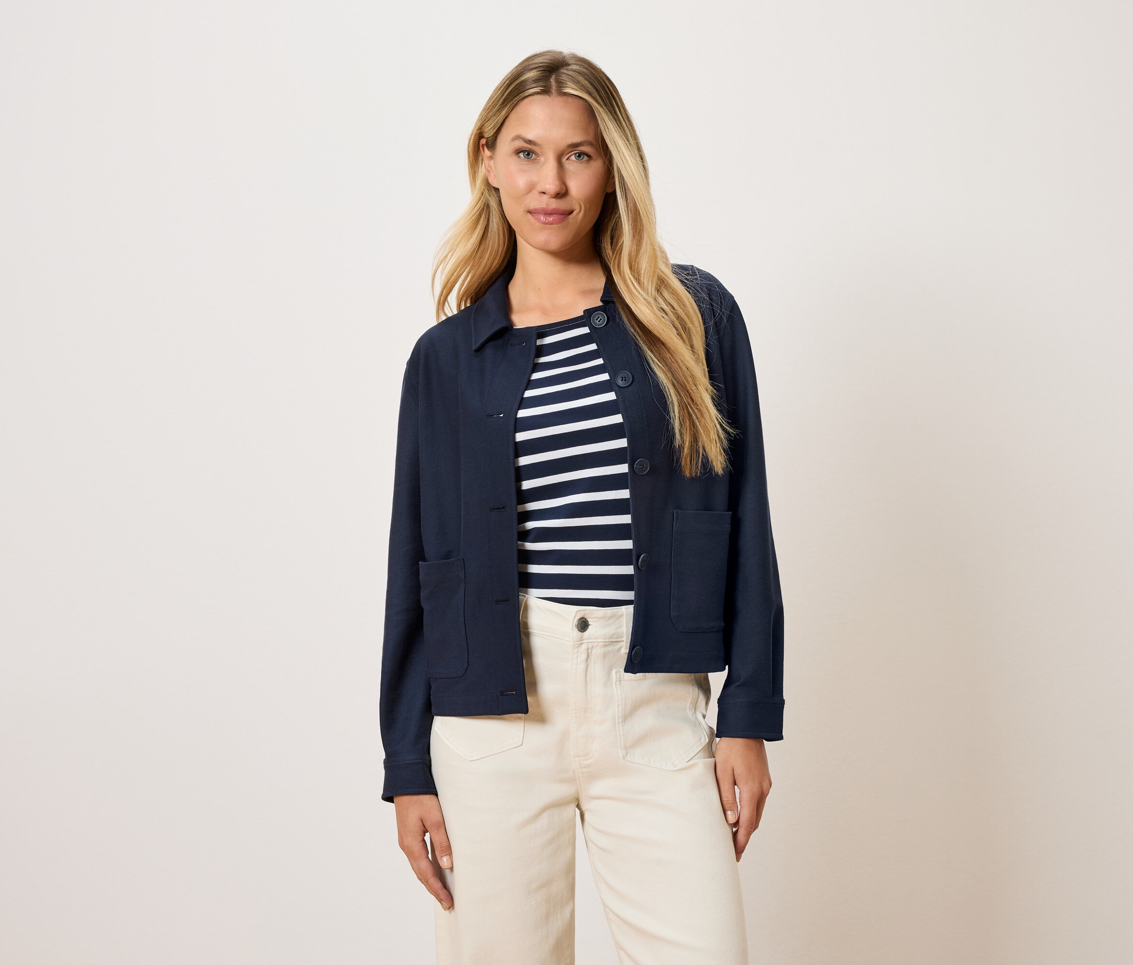 Frau trägt eine marineblaue Jacke über einem gestreiften Oberteil und cremefarbene Hosen.