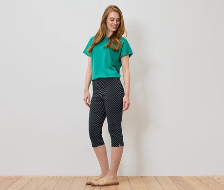Frau mit langen, roten Haaren, die ein grünes T-Shirt und eine dunkle Caprihose mit geometrischem Muster trägt.