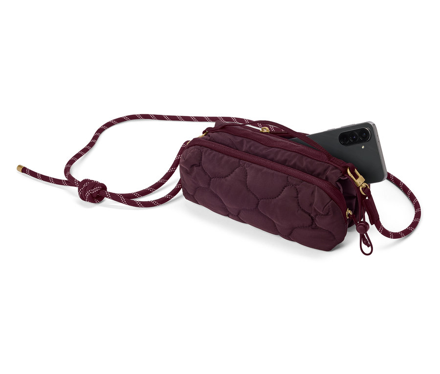 Eine gesteppte, burgunderrote Tasche mit Kordelriemen und einem schwarzen Smartphone, das aus der Tasche ragt.