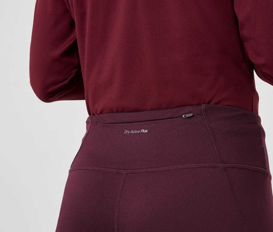 Nahaufnahme von einer Person, die ein weinrotes, langärmeliges Oberteil und Leggings mit der Aufschrift "Dry Active Plus" trägt.