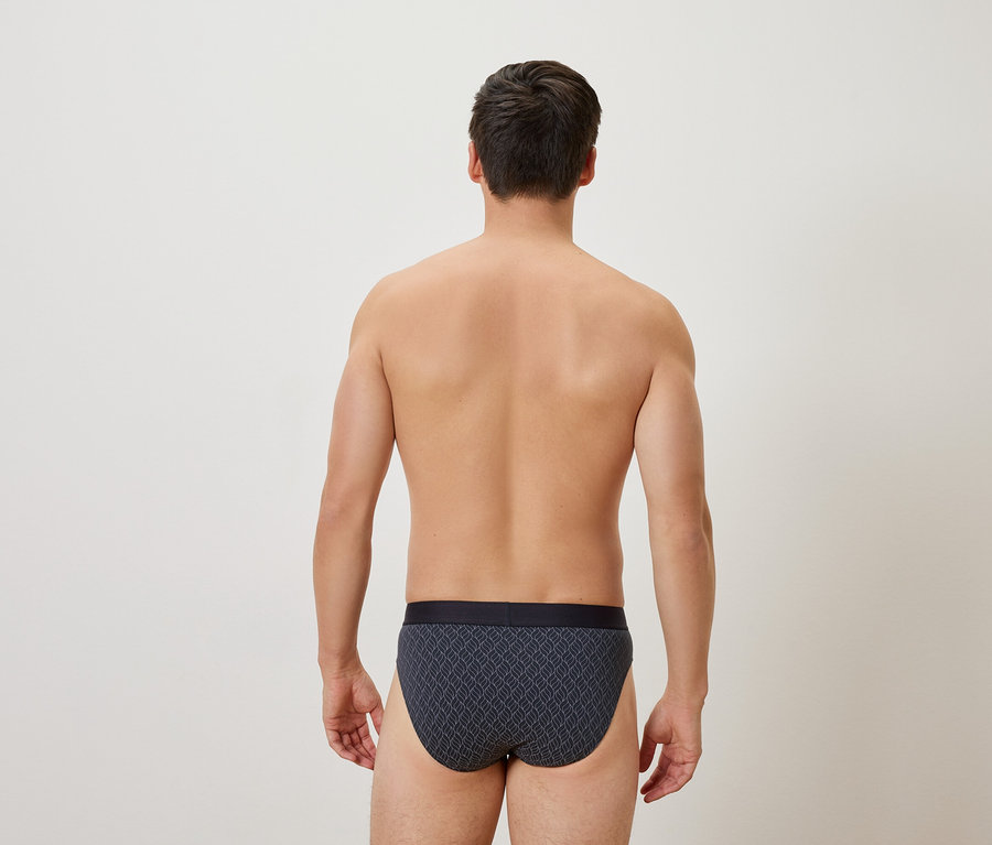 Rückansicht eines Mannes mit gemusterter Unterhose vor einem neutralen Hintergrund.