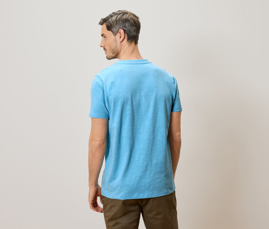 Mann von hinten in hellblauem T-Shirt und braunen Hosen.