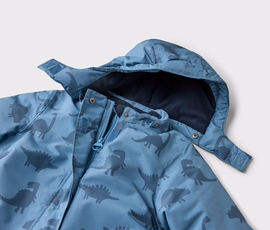 Nahaufnahme einer blauen Jacke mit Kapuze und Dinosaurier-Muster, die teilweise geöffnet ist und ein marineblaues Fleecefutter zeigt.