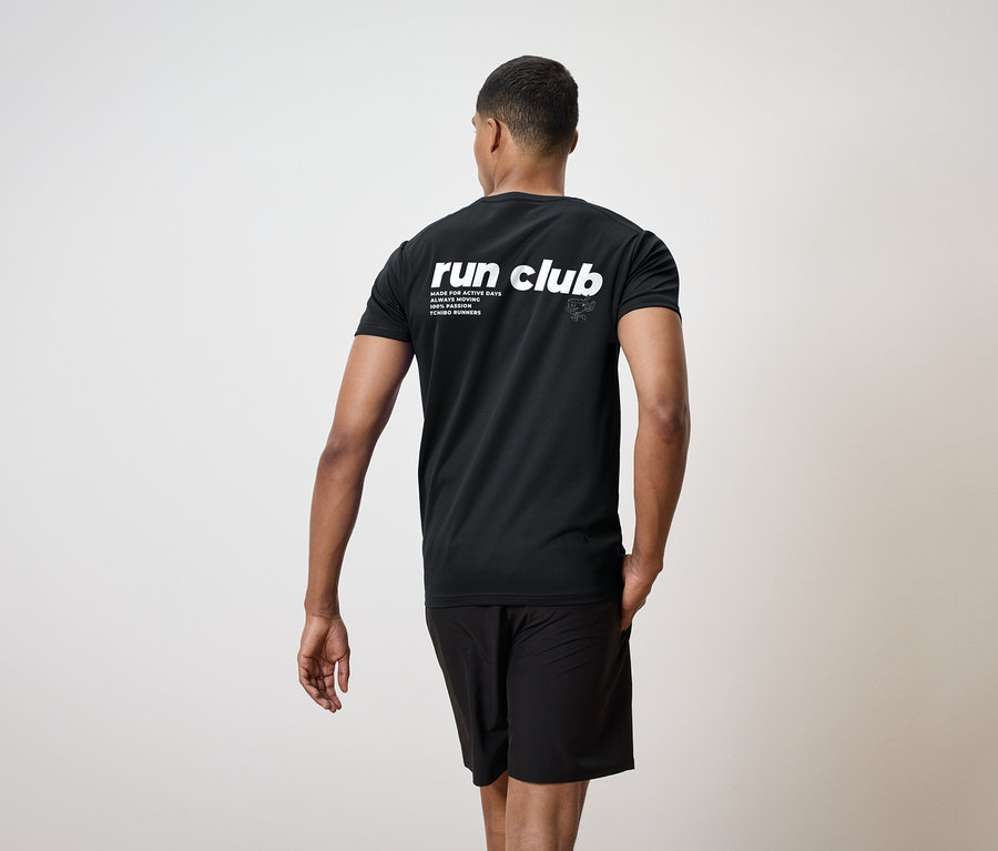 Ein Mann von hinten, bekleidet mit einem schwarzen T-Shirt mit der Aufschrift "run club" und schwarzen Shorts.