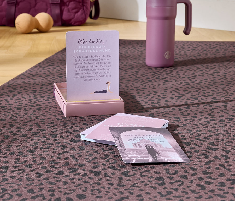 Auf einer gemusterten Matte liegen Yogakarten, eine Wasserflasche und eine Tasche im Hintergrund.
