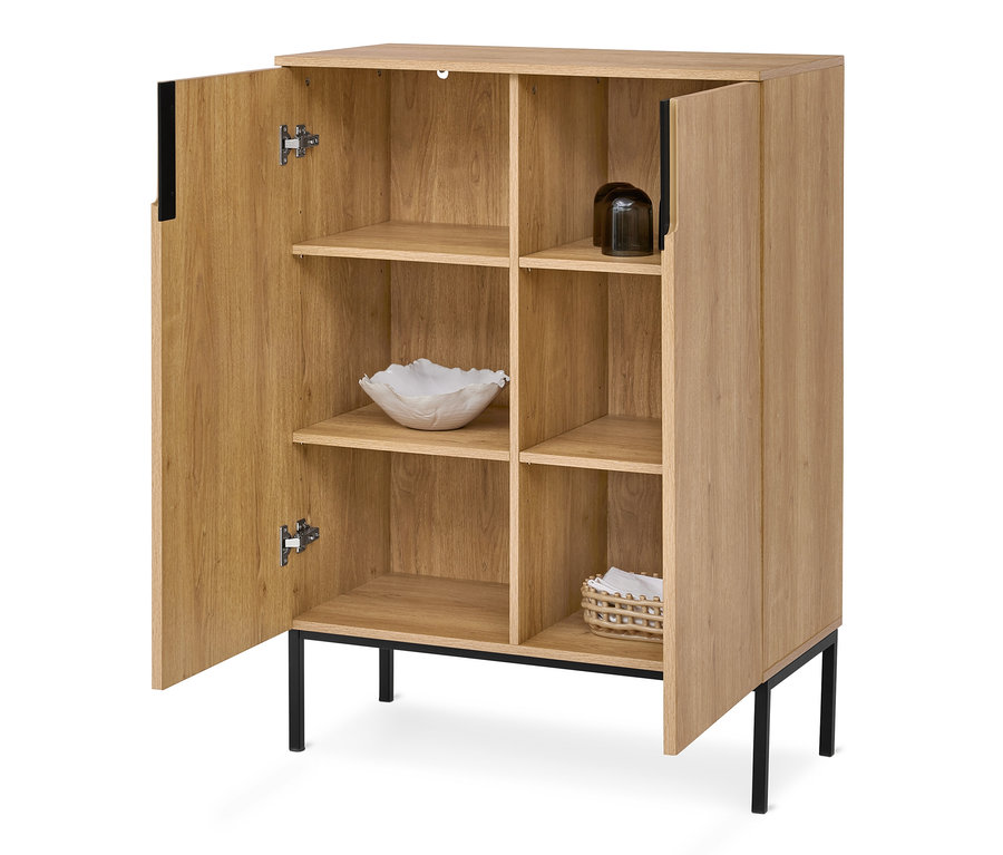 Helles Holzregal mit schwarzen Metallbeinen und Griffen, eine Tür ist offen und zeigt mehrere Fächer. Innen sind eine weiße Dekoschale, zwei dunkle Gläser und ein kleiner geflochtener Korb zu sehen.