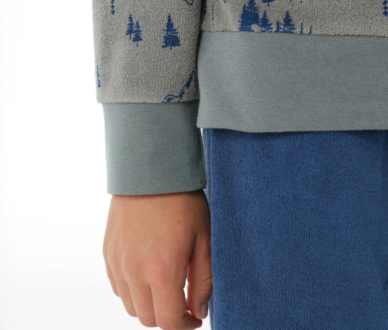 Kind trägt SCHIESSER Kinder-Pyjama mit Bündchen: graues Oberteil mit blauen Baummotiven und blaue Hose.