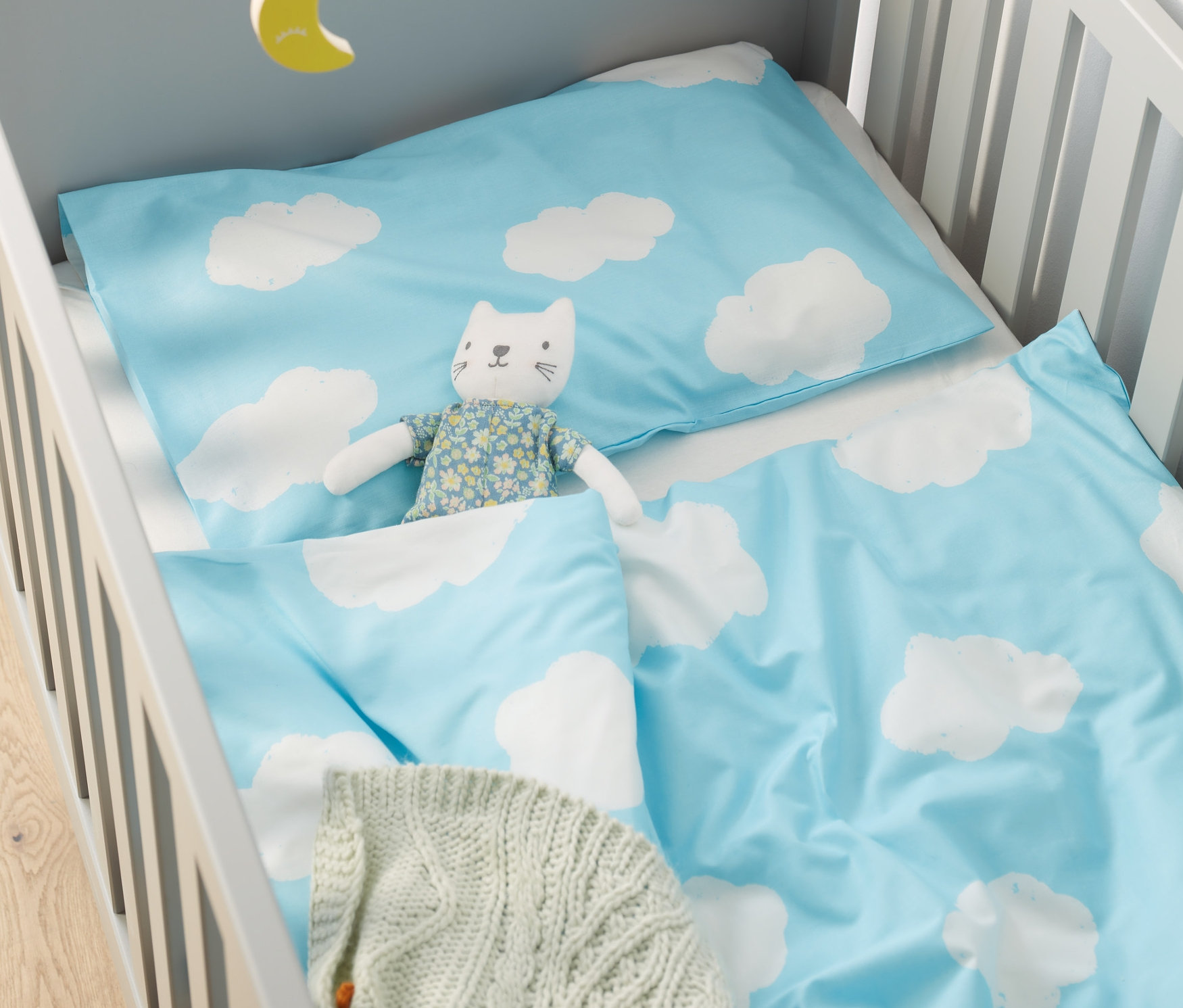 Babybett mit Baby-Bettwäsche mit Wolkenmuster und Katzenspielzeug.