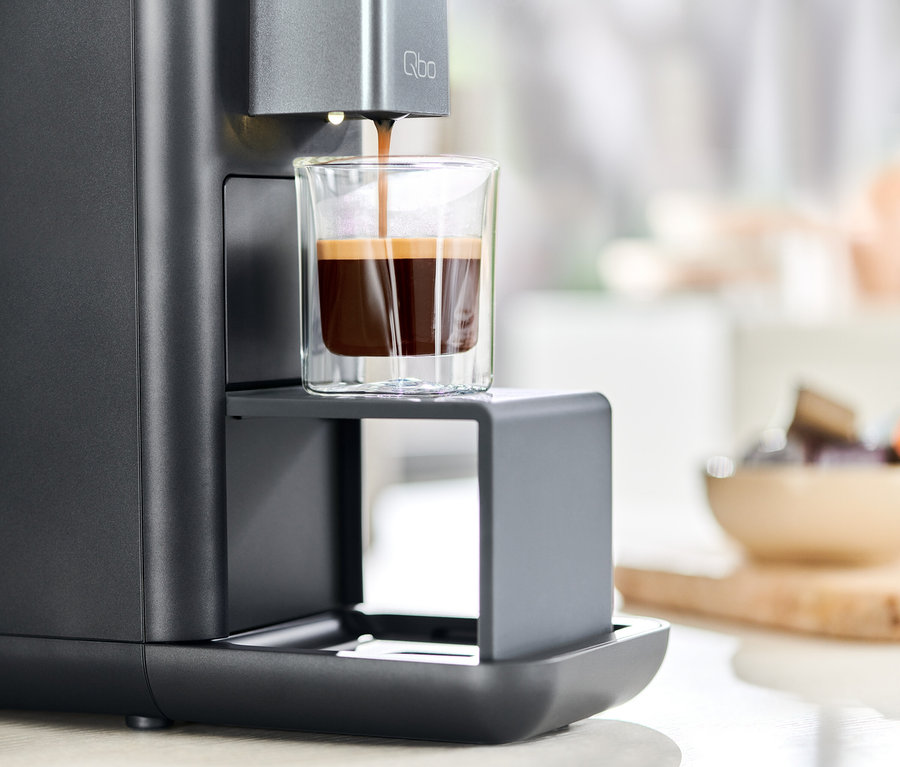 Kaffee wird aus einer Qbo ESSENTIAL Dark Stone Kaffeemaschine in ein Glas gegossen.