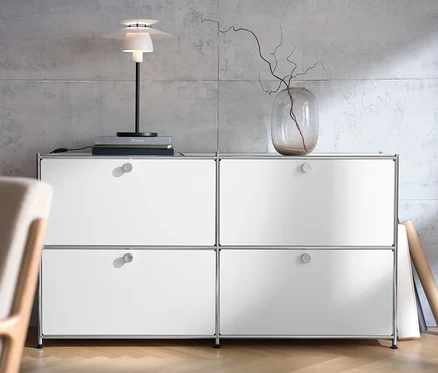 Weißes Sideboard »CN3« mit vier Klappen, darauf eine Tischleuchte aus Metall und eine Vase mit Zweigen.