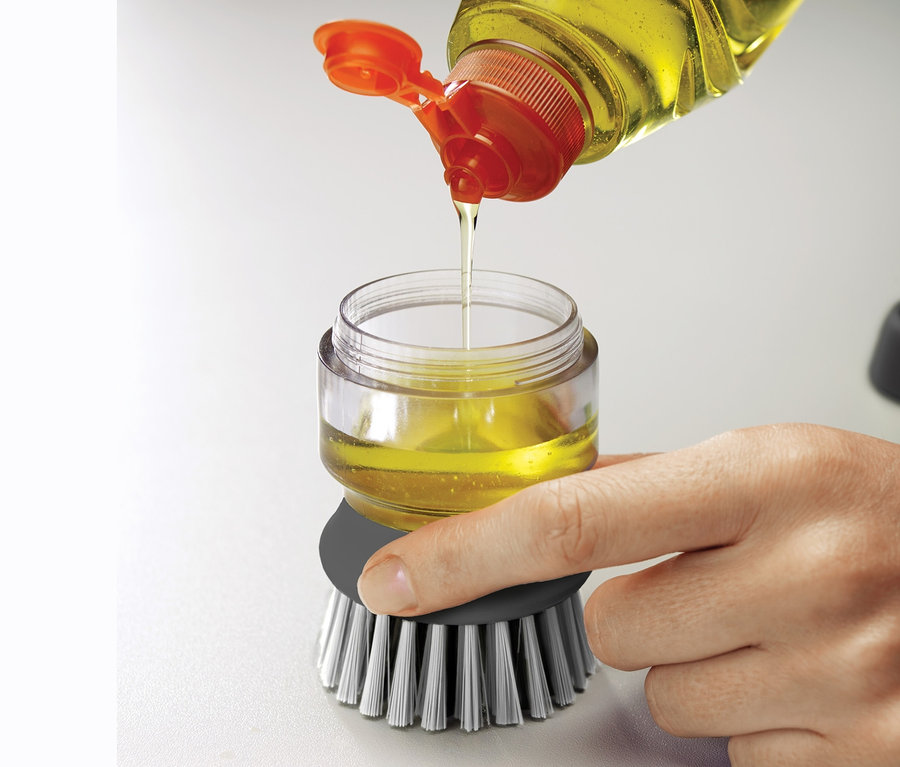 Person füllt gelbes Spülmittel in die Joseph Joseph Spülbürste mit Spülmittelspender.