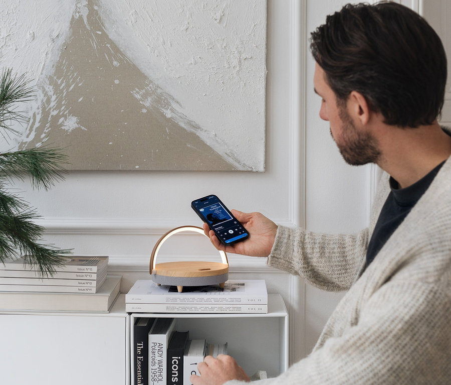 Mann hält Handy über Bluetooth®-Lautsprecher mit kabellosem Ladegerät und LED-Nachtlicht.