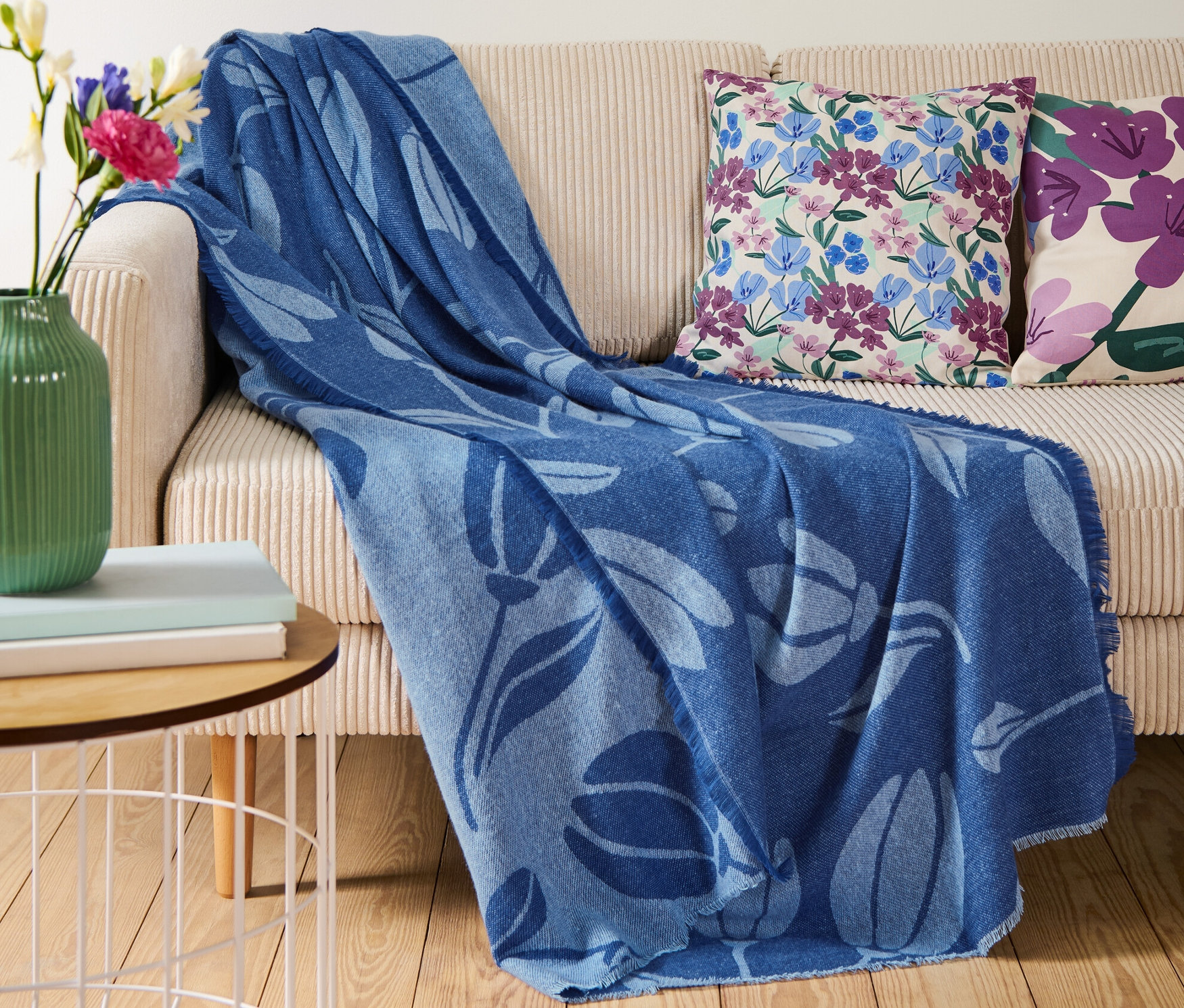 Auf einem beigen Sofa liegt eine blaue Wohndecke mit Fransen.