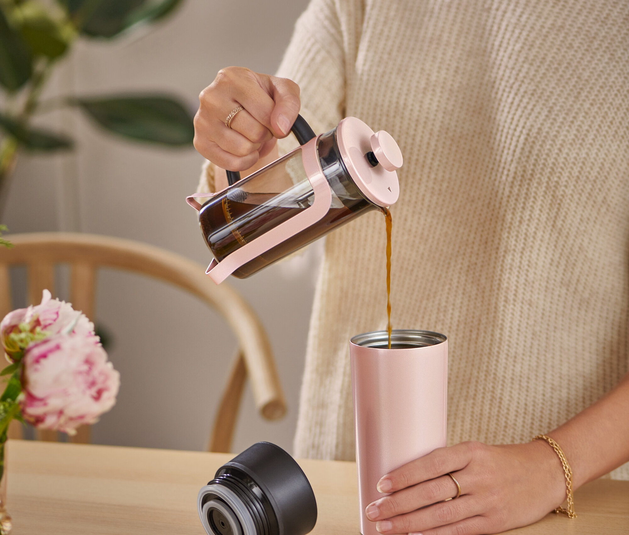 Frau gießt Kaffee aus einer Siebstempelkanne in einen Coffee-to-go-Becher.