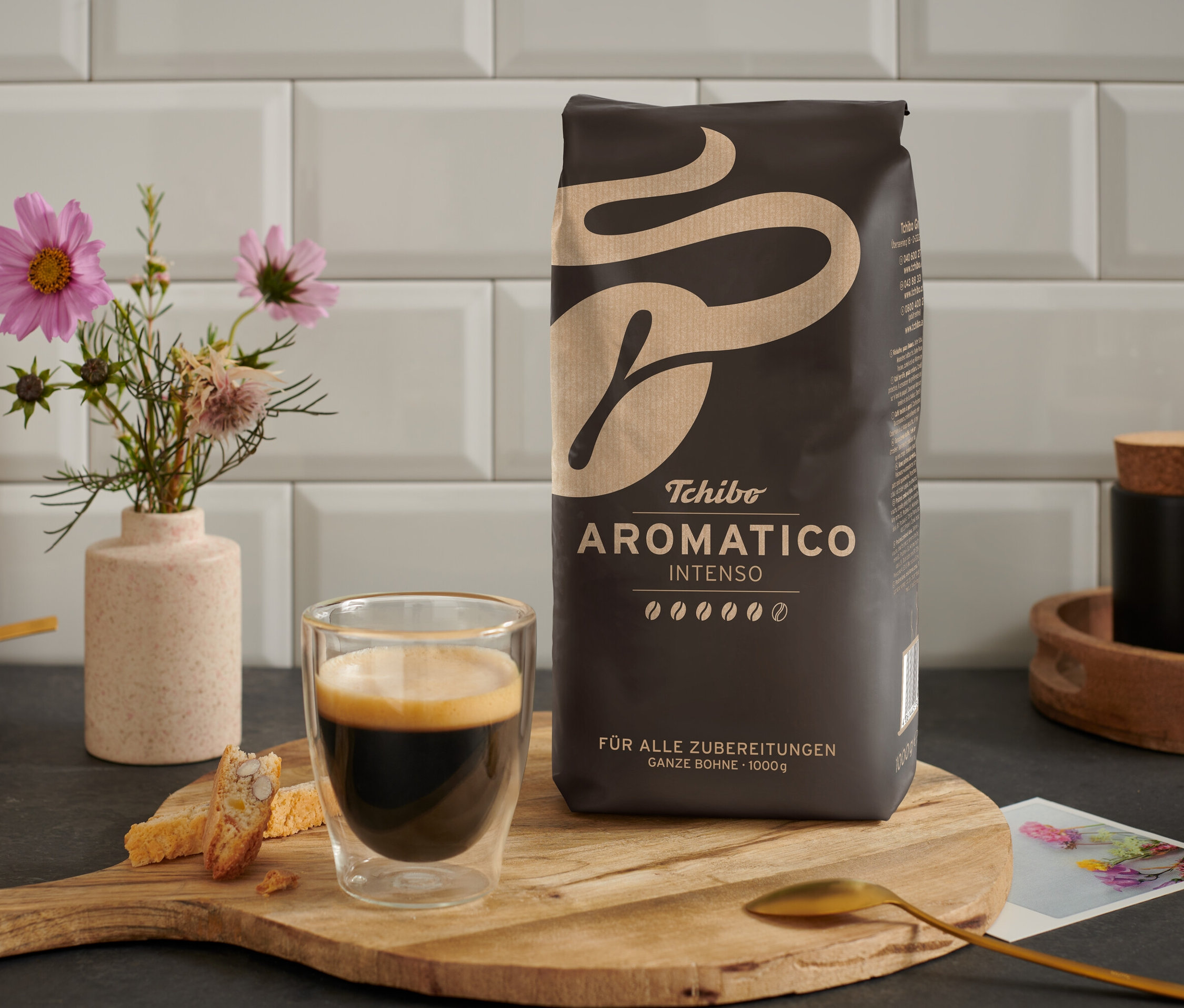 Eine Tasse Kaffee steht neben einer Packung Aromatico Intenso - 1 kg Ganze Bohne auf einem Holztisch.
