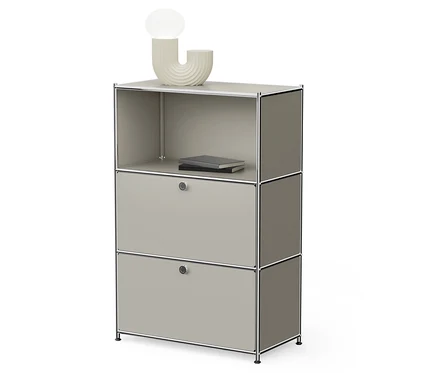 Grauer modularer Schrank mit zwei Schubladen und einem offenen Regal oben, auf dem ein Buch liegt und eine Lampe steht.