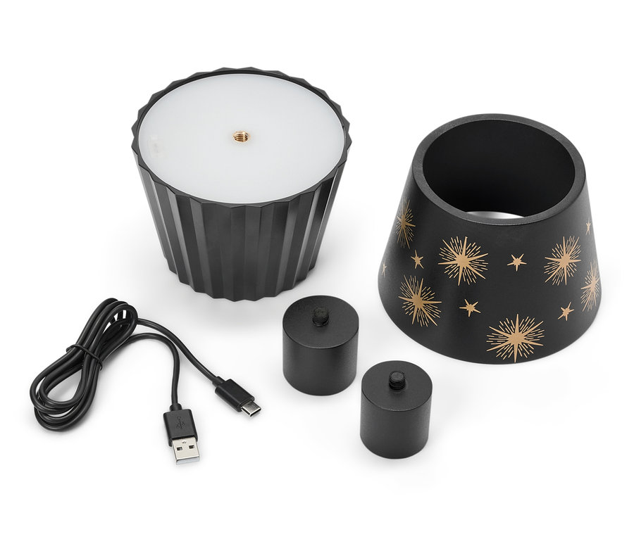 Eine schwarze Lampe mit Sternen, zwei schwarze Kerzen und ein USB-Kabel liegen auf einem weißen Hintergrund.