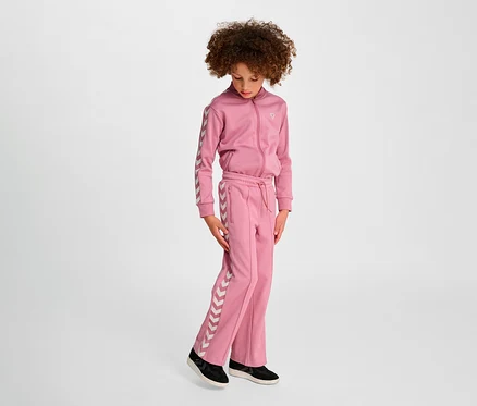 Mädchen in rosa Hummel HMLJR Archive Wideleg Poly Pants Anzug steht vor hellem Hintergrund.