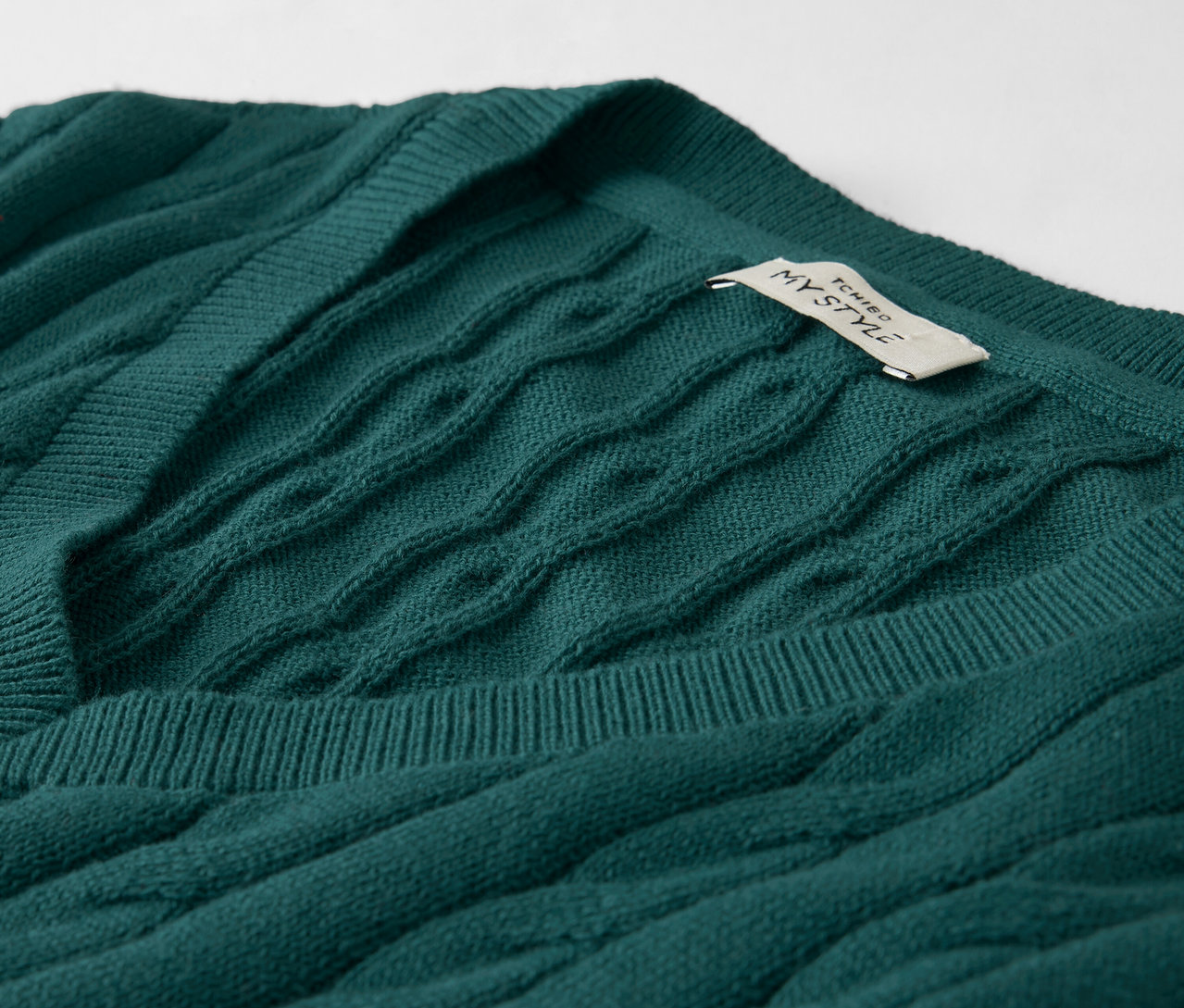 Nahaufnahme eines smaragdgrünen Zopfmuster-Pullovers mit V-Ausschnitt und einem Etikett.