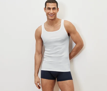 Ein lächelnder Mann posiert vor einem weißen Hintergrund und trägt ein weißes Doppelripp-Top und dunkelblaue Boxershorts.