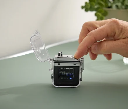 Eine Hand drückt einen Knopf an einem kleinen, schwarzen Gerät mit einem transparenten Gehäuse.