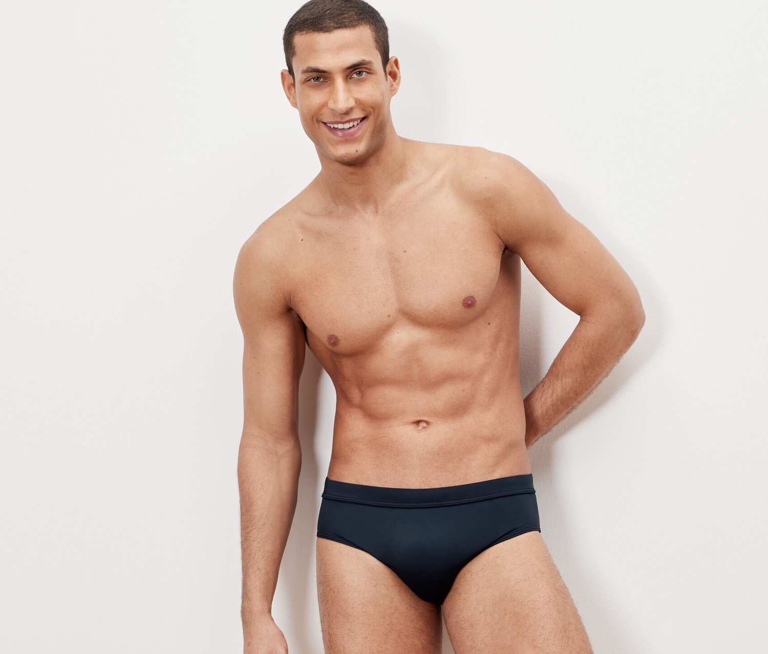 Mann posiert vor einem weißen Hintergrund in Badehose.