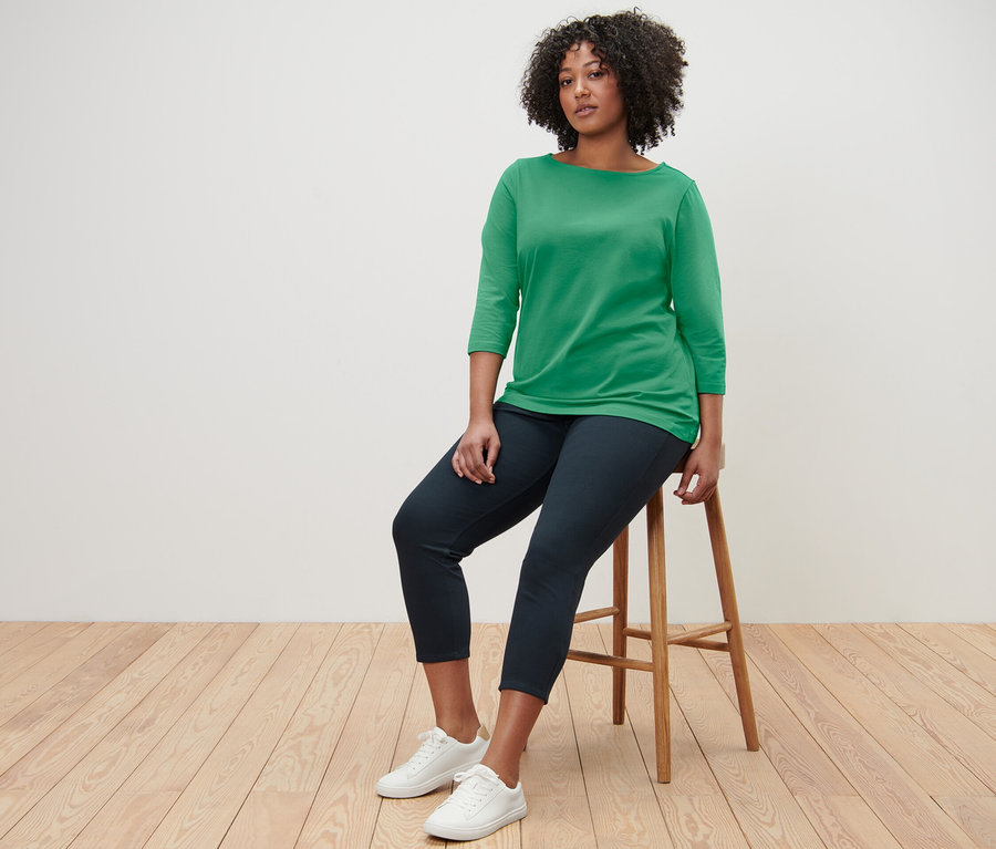 Frau sitzt auf einem Hocker und trägt ein grünes Shirt mit 3/4-Arm.
