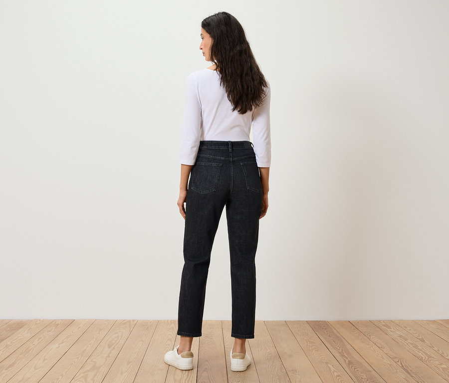 Frau steht mit dem Rücken zur Kamera, trägt ein weißes Dreiviertelarm-Shirt und schwarze Jeans.