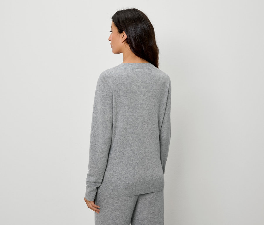 Rückansicht einer Frau mit dunklen Haaren in einem grauen Pullover und einer Hose.