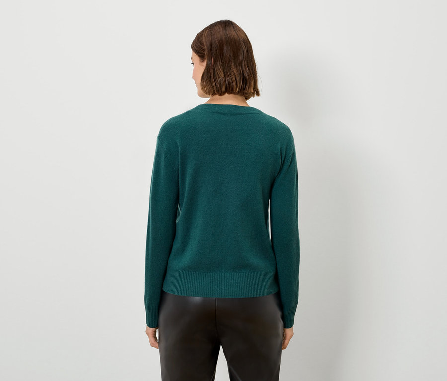 Frau von hinten, trägt einen grünen Pullover und eine schwarze Hose.