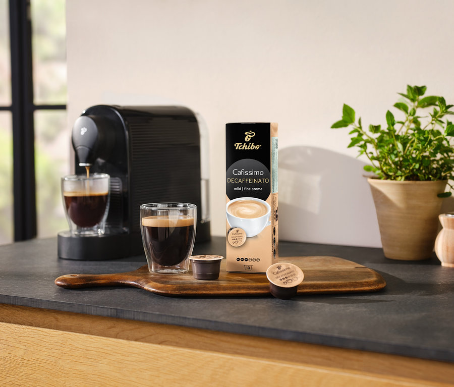 Kaffeemaschine gießt Kaffee in ein Glas neben einer Packung Cafissimo Decaffeinato - entkoffeiniert - 10 Kapseln.