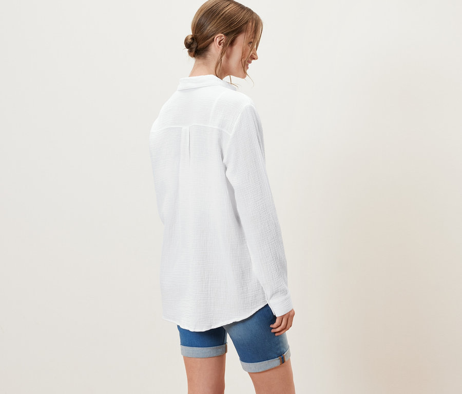 Frau trägt eine Musselin-Bluse, weiß, und Jeansshorts.