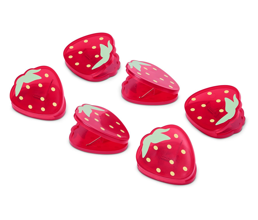 Sechs rote Erdbeer-förmige Klammern liegen auf einer weißen Oberfläche.