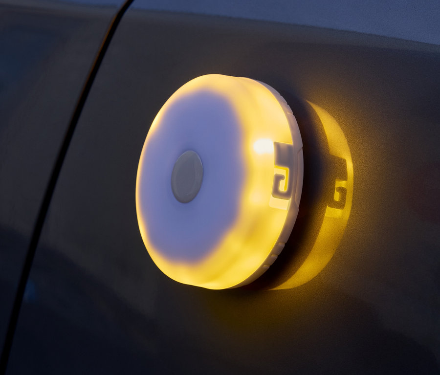Eine runde, batteriebetriebene Leuchte mit gelbem Licht ist an einer dunklen Oberfläche befestigt.