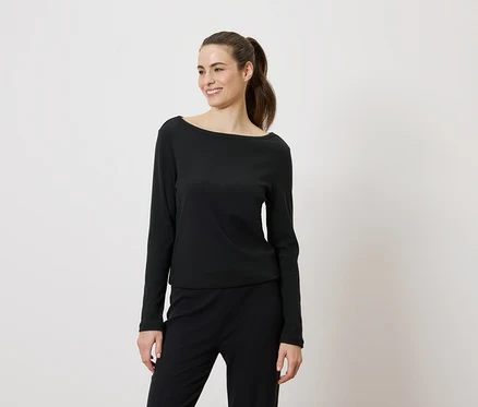 Frau mit Pferdeschwanz, die ein schwarzes Langarmshirt und eine schwarze Hose trägt und lächelt.