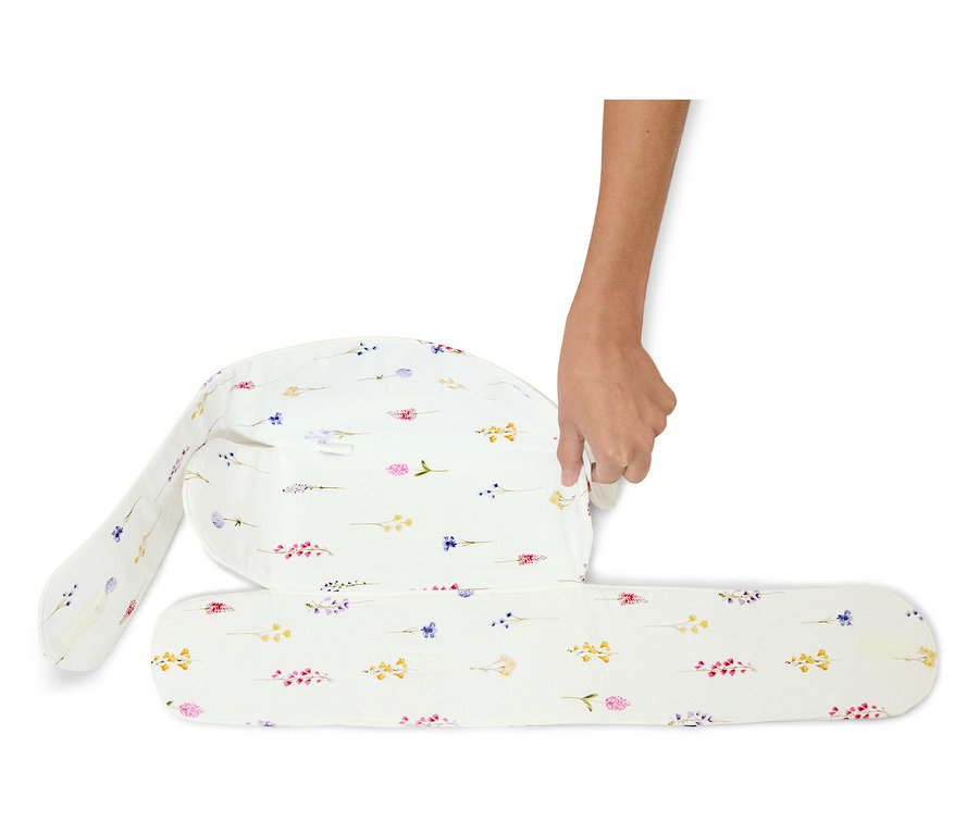 Eine Hand faltet ein weißes Stillkissen mit Blumenmuster.