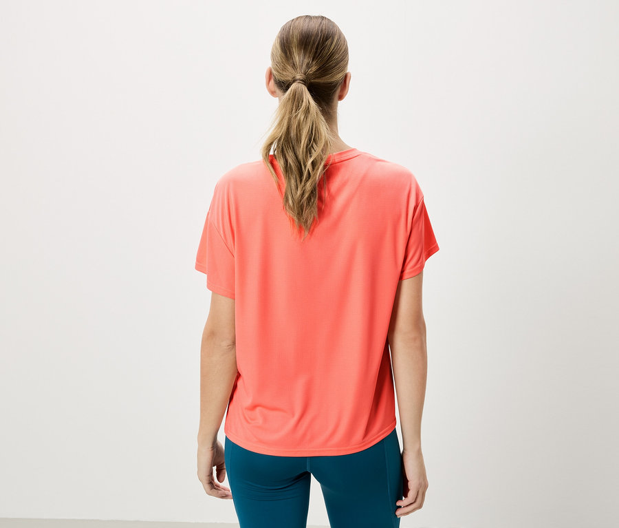Frau von hinten, trägt ein korallfarbenes T-Shirt und blaue Leggings vor einem weißen Hintergrund.