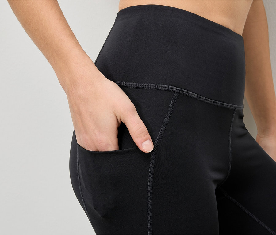 Frau steckt Hand in die Tasche einer schwarzen Leggings.