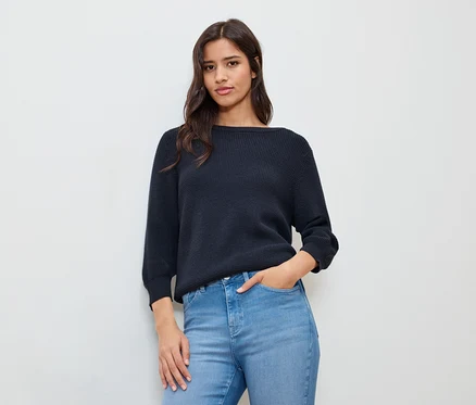 Frau mit einer Hand in der Hosentasche, trägt einen dunkelblauen Feinstrickpullover.