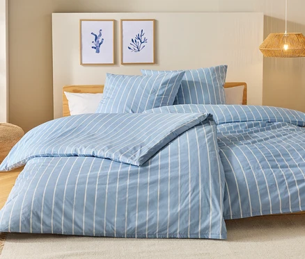 Bett mit blau-weiß gestreifter Bettwäsche, zwei Kissen und zwei Bilder an der Wand.