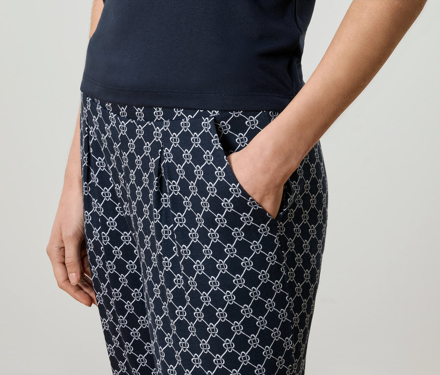 Nahaufnahme einer Frau, die marineblaue, gemusterte Hose und ein marineblaues Oberteil trägt und ihre Hand in der Hosentasche hat.