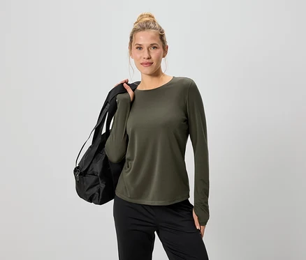 Frau mit Dutt trägt ein olivgrünes Langarmshirt und schwarze Hose, mit einer schwarzen Sporttasche über der Schulter.