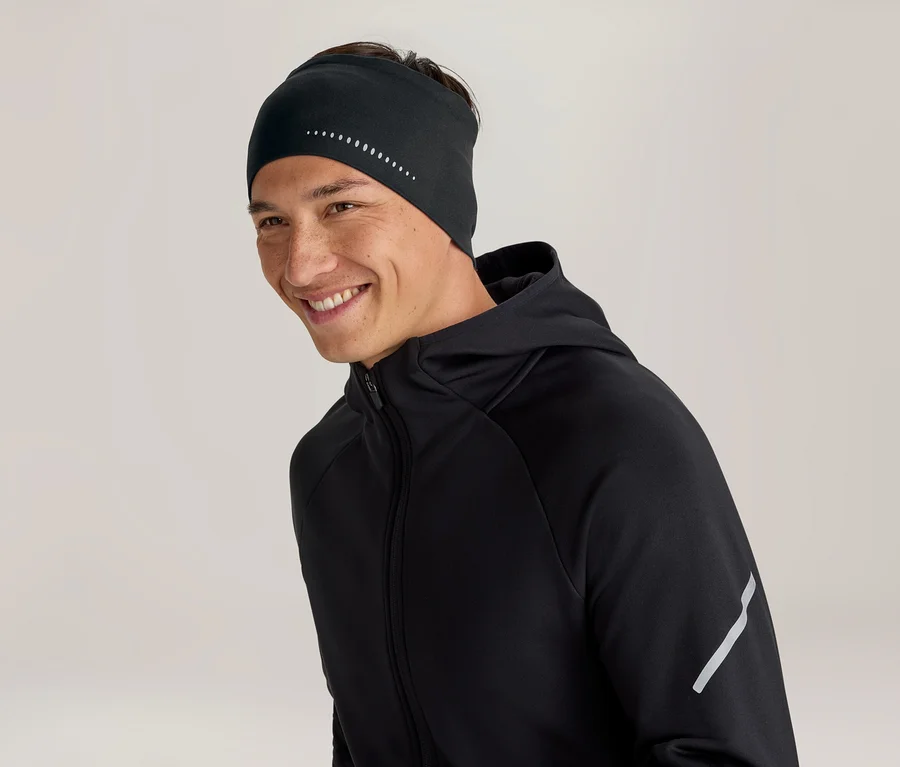 Lächelnder Mann trägt ein schwarzes Stirnband mit reflektierenden Punkten und eine schwarze Kapuzenjacke mit einem reflektierenden Streifen am Ärmel.