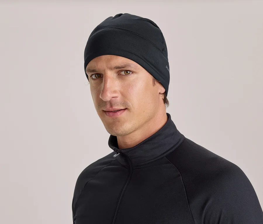 Ein Mann trägt eine schwarze Mütze und ein schwarzes Langarmshirt mit Stehkragen und Reißverschluss und blickt in die Kamera.