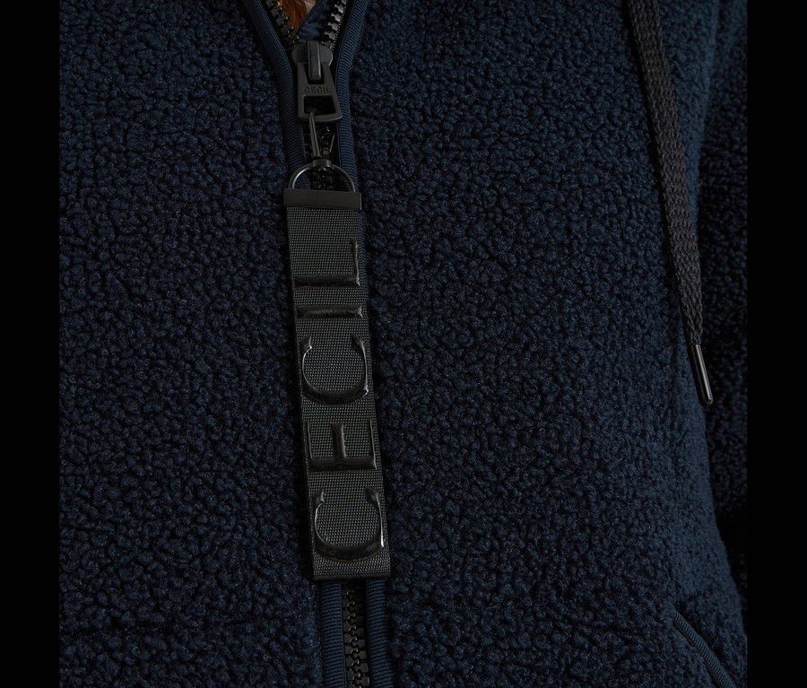 Nahaufnahme einer dunkelblauen CECIL Jacke aus flauschigem Teddy-Material, mit Reißverschluss, Zipper-Anhänger und Stoffetikett mit CECIL-Logo.