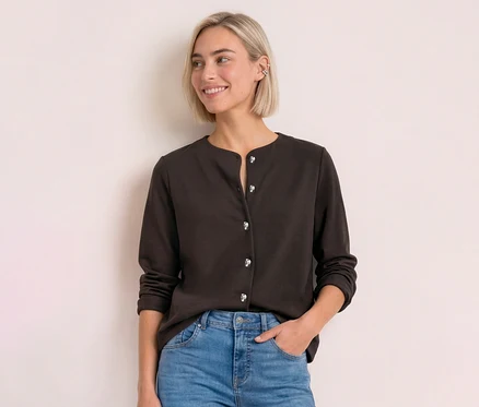 Junge Frau mit blondem Bob trägt einen dunkelbraunen Street One Cardigan mit silbernen Knöpfen und Jeans, lächelt zur Seite.